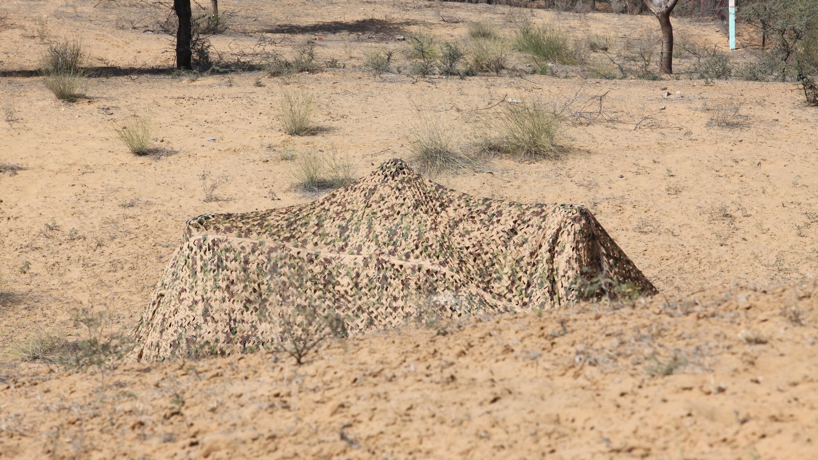 CAMPRO multi-spectral camouflage net deployed over equipment, showing three-dimensional garnish and shape disruption